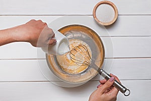 Woman`s hands close-up mixing eggs and sugar with wisk in a large bowl and pouring milk