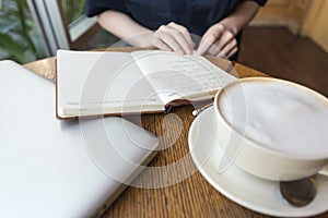 Woman`s hands with coffee cup, laptop and notebook taking notes for business on table, close up