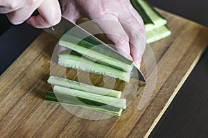 Woman`s Hands Cut Cucumber Matchsticks with Santoku Knife on a Wooden Chopping Board. Salads, Maki and Temaki Sushi Rolls