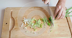 Woman`s hands cut with knife spring onion bunch on wooden cutting board