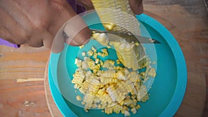 A woman\'s hands cut and thresh corn from the cobs using a sharp knife