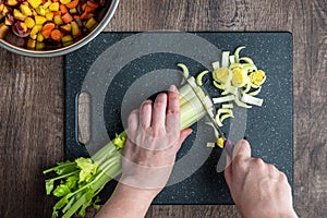 WomanÃ¢â¬â¢s hands cutting a bunch of celery, black cutting board and chef knife, bowl of diced rainbow carrots