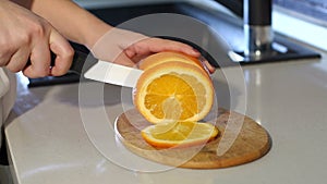Woman`s hands cutting fresh orange on kitchen. Slow motion. Close-up.