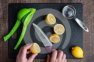 WomanÃ¢â¬â¢s hands cutting a lemon on a black cutting board, chef knife, green citrus squeezer, measuring cup