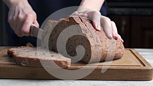 Woman's hands cutting whole grain wheat bread on wooden board.