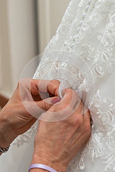 A woman's hands fasten in buttons of a bride's formal dress