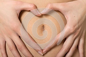 Woman's hands forming heart symbol around navel photo