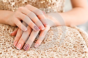 Woman& x27;s hands with french manicure and candy cane pattern on the nails. Christmas and New Year nail design. Beauty salon