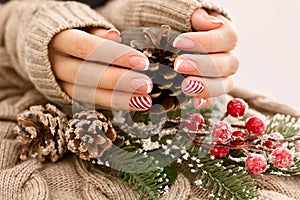 Woman& x27;s hands with french manicure and candy cane pattern on the nails. Christmas and New Year nail design. Beauty salon