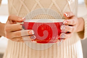 Woman& x27;s hands with french manicure and candy cane pattern on the nails. Woman with beautiful manicure holding big red