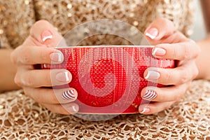 Woman& x27;s hands with french manicure and candy cane pattern on the nails. Woman with beautiful manicure holding big red
