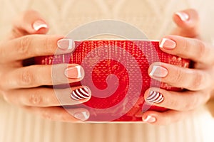 Woman& x27;s hands with french manicure and candy cane pattern on the nails. Woman with beautiful manicure holding big red