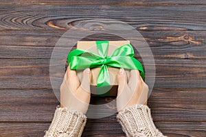 Woman`s hands give wrapped valentine holiday handmade present in craft paper with green ribbon. Present box, decoration of gift o