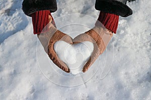 Woman's hands with gloves hold a heart made of snow