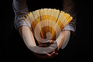 Woman`s hands with gluten free spaghetti made from rice and maize on dark background