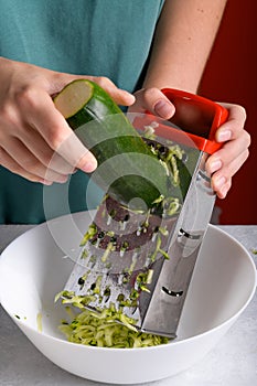 woman& x27;s hands grating green zucchini with a stainless steel hand grater, close up, food lifestyle