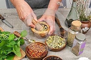 Woman`s hands grind cardamom in a wooden mortar. Kitchen gray table with various spices