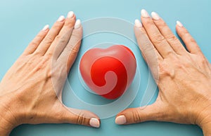 woman's hands guard a red heart on a blue background. the concept of women's health, life insurance, chronic diseases,