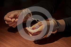 Woman's hands are handcuffed with metal handcuffs on the wooden surface of a table. Concept: capture or arrest.