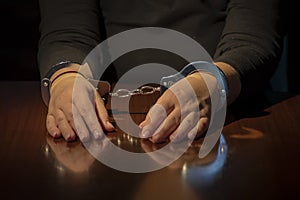 Woman's hands are handcuffed with metal handcuffs on the wooden surface of a table. Concept: capture or arrest.