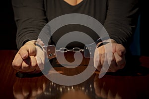 Woman's hands are handcuffed with metal handcuffs on the wooden surface of a table. Concept: capture or arrest.