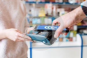 A woman`s hands are held by a payment terminal and a man pays for a purchase using a smartphone. Close up and side view. The