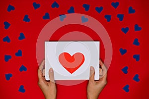 Woman`s hands hold card with red heart above red background