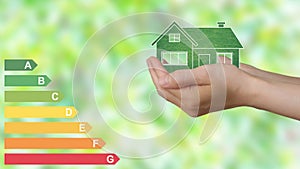 A woman's hands hold an eco green house, On the left energy efficiency graph.