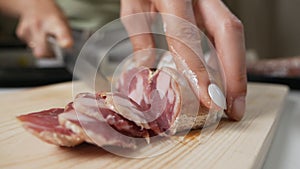 Woman`s hands hold a knife and cut sausage, salami into thin slices on a wooden board