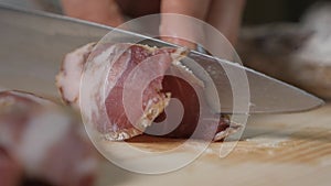 Woman`s hands hold a knife and cut sausage, salami into thin slices on a wooden board. Shooting close-up