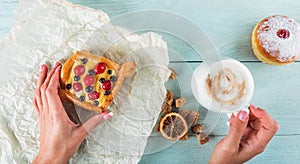 Woman`s hands hold a sweet pastrie with berries and coffee cup. Flat lay, top view photo