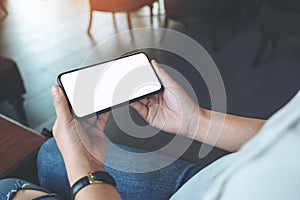 Woman`s hands holding black mobile phone with blank white screen horizontally in cafe