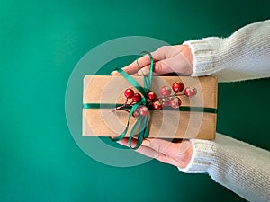 Woman`s hands holding a Christmas present on a green background