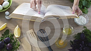 Woman's hands holding cooking book, girl choosing recipe and flipping pages