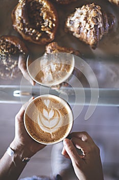 Woman`s hands holding a cup of signature coffee prepared by a barista next to a counter full of croissants. Restaurant. Quiet