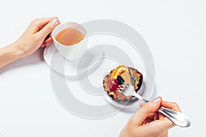 Woman's hands holding cup tea and fork to eat fruit dessert