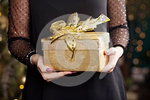 Woman`s  hands holding gold gift box. Christmas, new year, birthday concept. Festive background with bokeh and sunlight. Magic