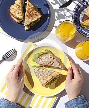 Woman`s hands are holding healthy vegetarian wheat bran sandwich on the yellow plate. Breakfast concept flat lay.