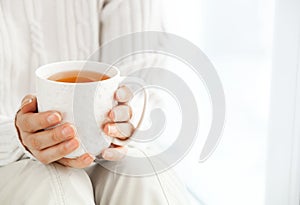 Woman`s hands is holding hot cup of coffee or tea in morning su