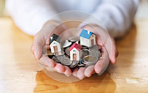 A woman`s hands holding house models and coins for saving money concept