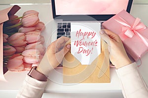 Woman`s hands holding a letter in craft envelope. Pink background, women`s day concept. Tulips flower and pink gift box in