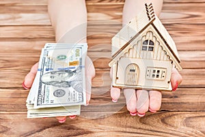 Woman`s hands holding money and model of house over wooden table