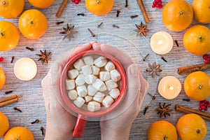 Woman`s hands holding mug of hot cocoa and marshmallows with festive flat lay arrangement