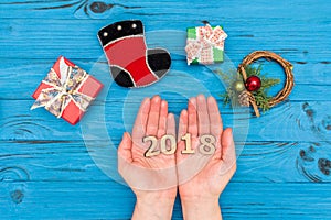 Woman`s hands holding numbers 2018 near gift boxes and New Year ornaments on blue old table