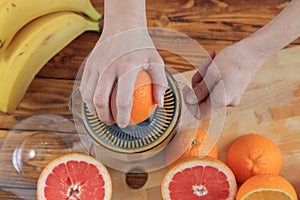 Woman`s hands is holding a orange half and making juice