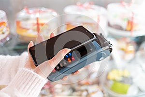 A woman`s hands is holding a payment terminal and paying for a purchase using a smartphone. Copy space. The concept of NFC,