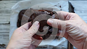 Woman`s hands holding and pulling apart a gooey fresh chocolate brownie