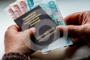 Woman`s hands holding russian pension certificate and russian rubles.