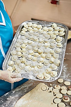 Woman`s hands holding a tray full of dumplings sprinkled with flour . Delicious homemade food