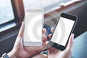 A woman`s hands holding two mobile phones with blank white screen in modern cafe